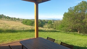 Une terrasse en bois avec une table et des chaises, donnant sur un champ verdoyant et des arbres.