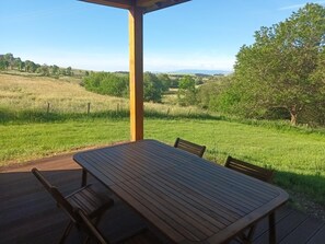 Eine Holzterrasse mit Tisch und Stühlen, mit Blick auf ein Wiesfeld und Bäume.