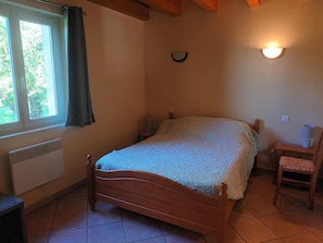 Une chambre à coucher avec un lit en bois, une fenêtre avec des rideaux, un luminaire fixé au mur et un radiateur.