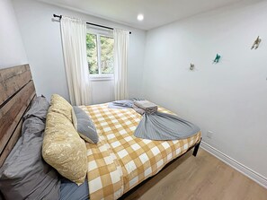 A bedroom with a checkered bedspread, a wooden headboard, and a window with curtains.