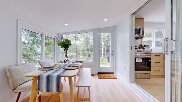 A modern dining area with a long table, benches, and a view of the outdoors. - Modern Lakefront Escape In Muskoka (Emsdale)