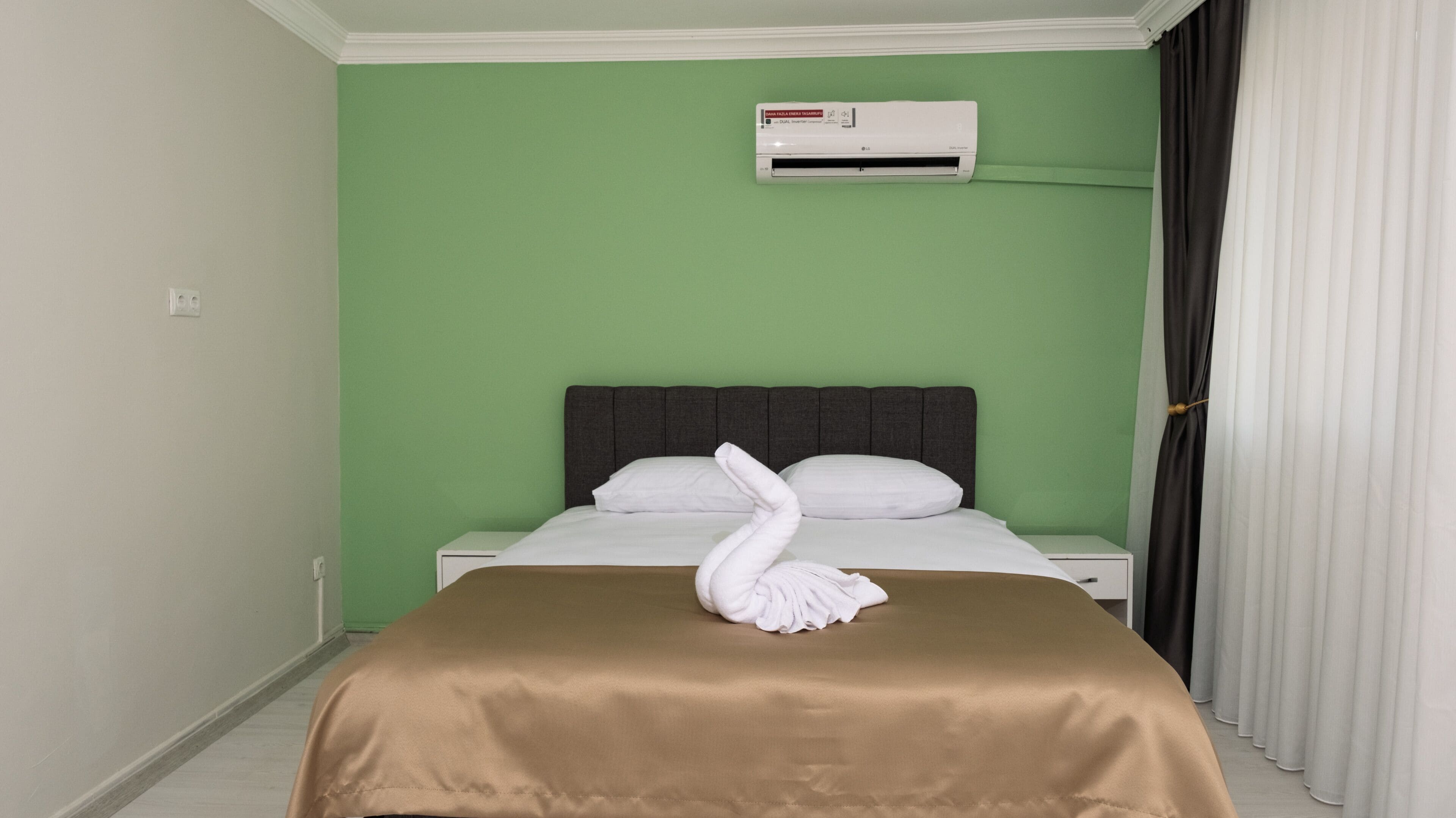 A hotel room with a bed, a wall-mounted air conditioner, and a curtain.