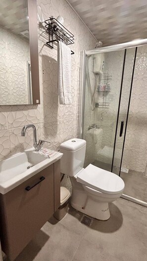 Un baño con un lavamanos blanco, inodoro y cabina de ducha con mampara de vidrio.
