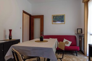 A dining area with a table set for two, a red sofa, and a framed artwork on the wall. - Appartamento Magnolia - Affitti Brevi Italia (Borghetto Santo Spirito)