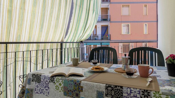 Un balcon avec une table dressée pour deux personnes, agrémenté d’un livre, d’une assiette de pâtisseries, d’une cafetière et d’une tasse.