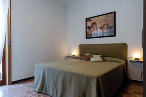 A hotel room with a bed, two bedside lamps, a painting on the wall, and a window with curtains. - Appartamento Magnolia - Affitti Brevi Italia (Borghetto Santo Spirito)