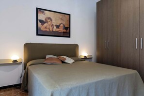 Een slaapkamer met een bed, twee bedlampen, een nachtkastje, een garderobe en een lijst met een afbeelding aan de muur.