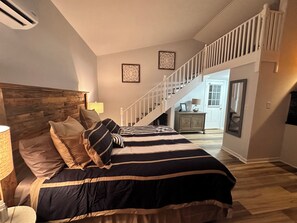 A bedroom with a large bed, a wooden headboard, a staircase leading to another room, and a nightstand with a lamp. -  1-bedroom and Loft pool house apartment with private pool /lake Louisville TN (Louisville)