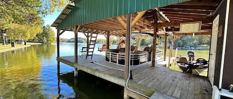 Un muelle techado con un barco, cubierta de madera y vista a un lago.