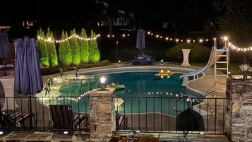 Une piscine bordée d’un muret en pierre, avec des chaises longues et des guirlandes lumineuses.