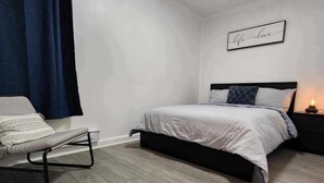 A bedroom with a bed, a bedside table with a lamp, a chair, and a wall with a sign. - Montreal Rental 2 BRs/ Full Bathroom (Montréal)