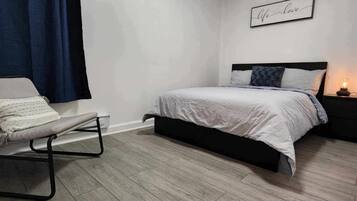 Une chambre à coucher avec un lit, une table de chevet avec une lampe, une chaise et un mur orné d’une affiche.