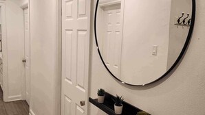 A hallway with white doors, a round mirror, and a black shelf with potted plants. - Montreal Rental 2 BRs/ Full Bathroom (Montréal)