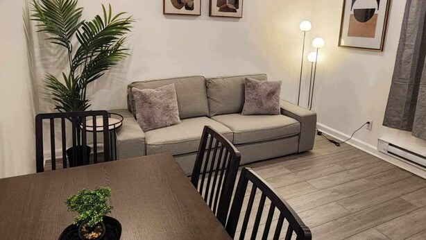A modern living room with a sofa, a dining table with chairs, a potted plant, and abstract art on the walls. - Montreal Rental 2 BRs/ Full Bathroom (Montréal)