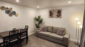 A living room with a dining table, chairs, a sofa, a floor lamp, and wall art. - Montreal Rental 2 BRs/ Full Bathroom (Montréal)