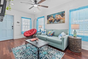 A living room with a teal sofa, a red chair, a coffee table, and a painting of sea turtles. - Turtle Nest Condo + Pool / 2nd Floor (Key West)