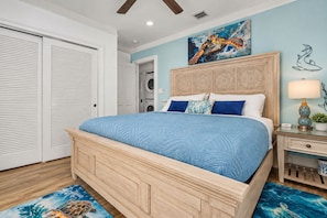 A bedroom with a wooden bed, a nightstand, a wall-mounted lamp, and a painting of a sea turtle. - Turtle Nest Condo + Pool / 2nd Floor (Key West)