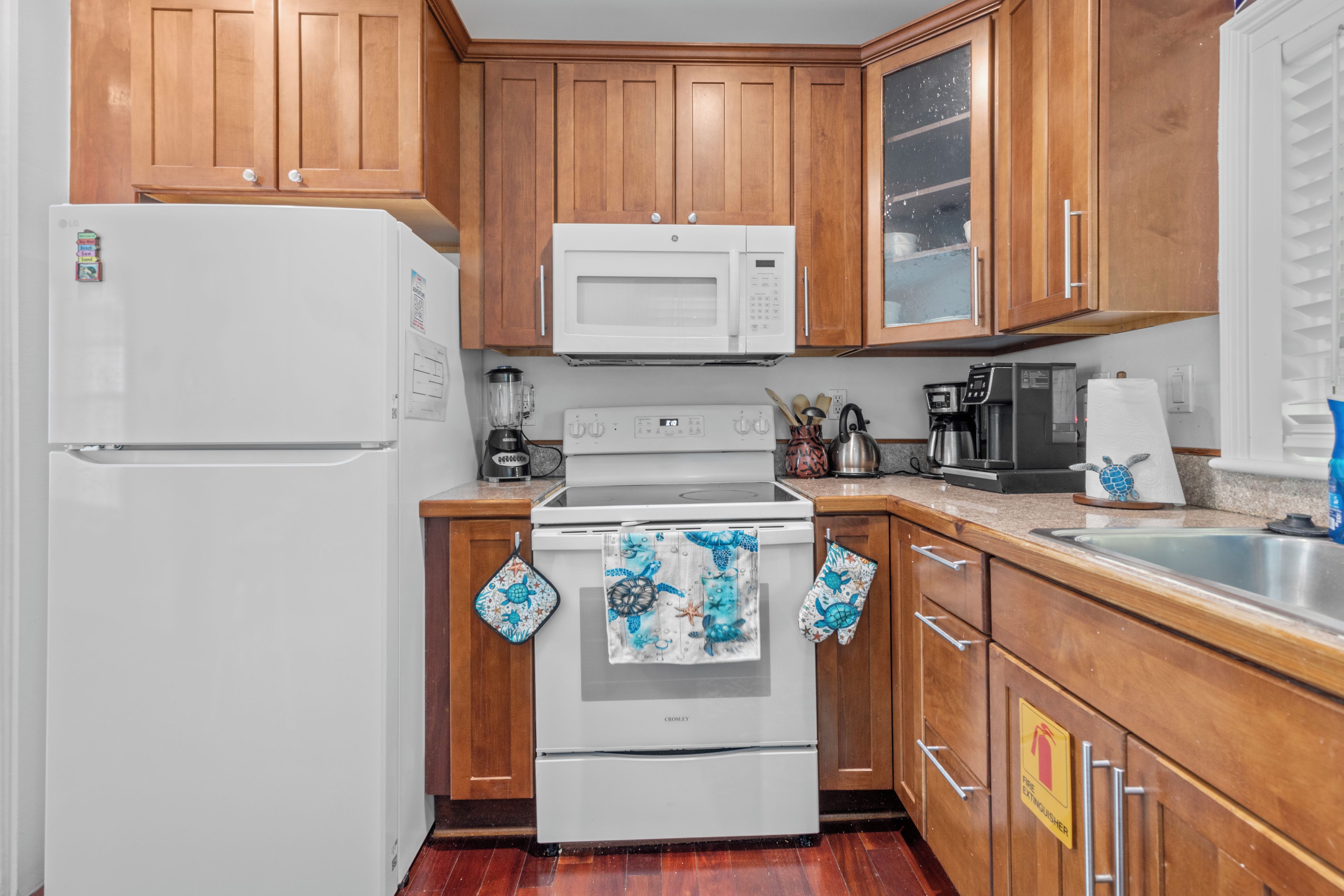 Una cocina con armarios de madera, un refrigerador blanco, un microondas, una estufa y una cafetera.