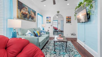 Una sala de estar con un sofá azul turquesa, una silla roja y un tapiz estampado.