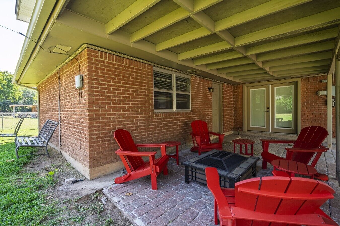 Un patio couvert avec des fauteuils Adirondack rouges et une table, des murs en briques et une porte-fenêtre coulissante.