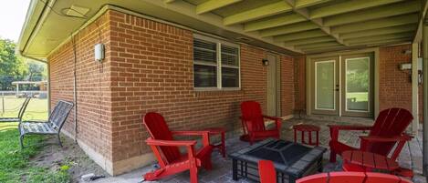 Un patio couvert avec des fauteuils Adirondack rouges et une table, des murs en briques et une porte-fenêtre coulissante.