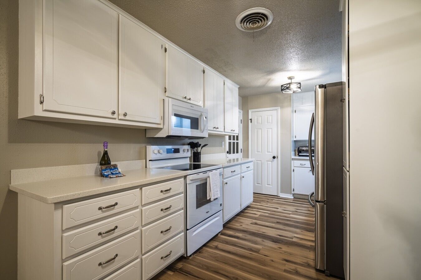 A kitchen with white cabinets, a microwave, an oven, and a refrigerator.