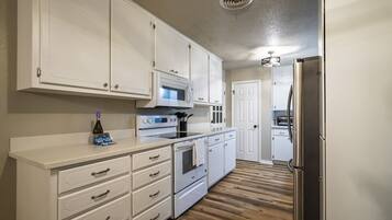 A kitchen with white cabinets, a microwave, an oven, and a refrigerator.