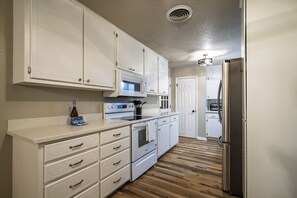 A kitchen with white cabinets, a microwave, an oven, and a refrigerator. - The Murf | Pet-Friendly OU Campus Sleeps 10 (Norman)
