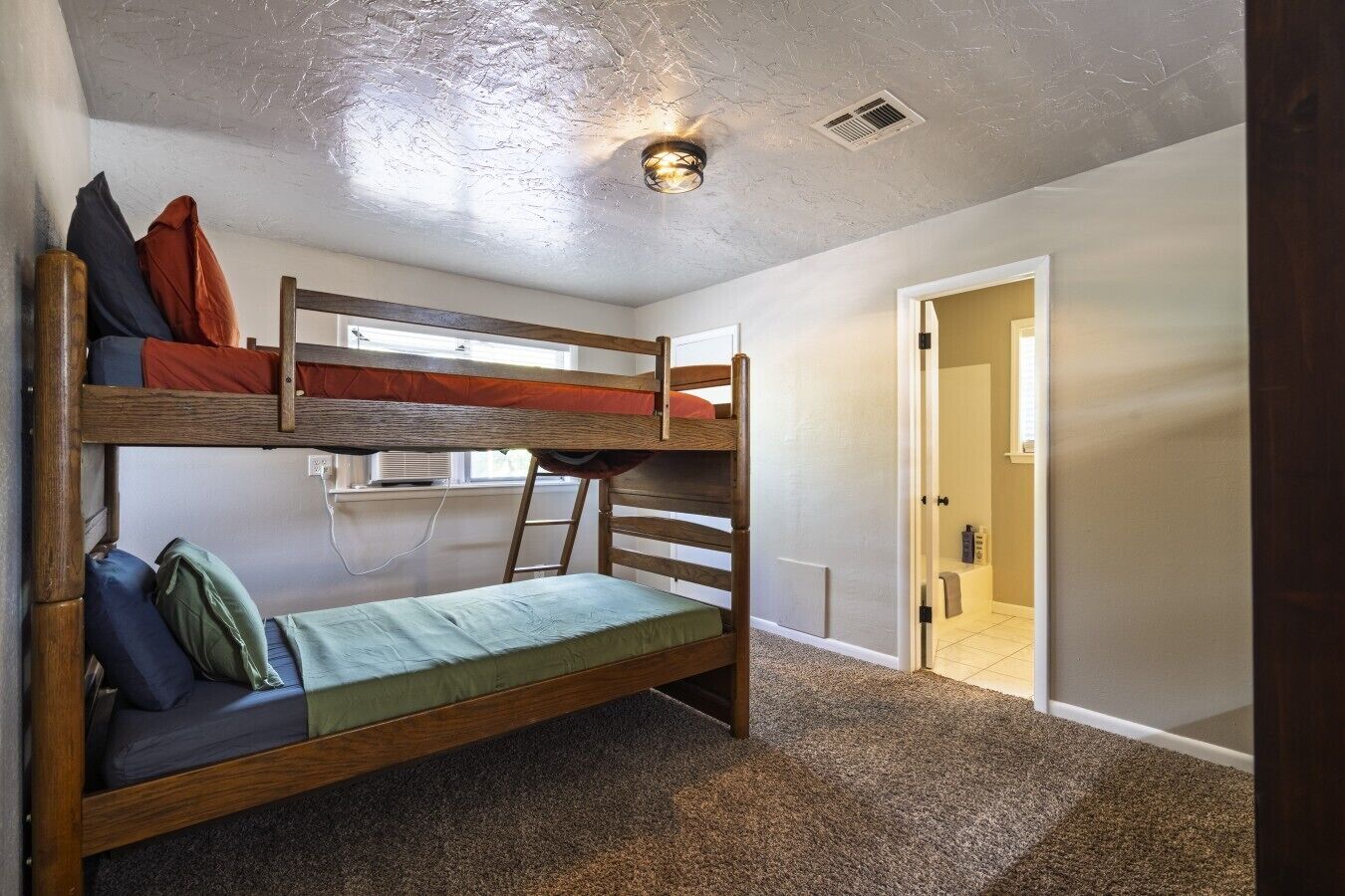 A bunk bed room with a ladder, a window, and a door leading to a bathroom.