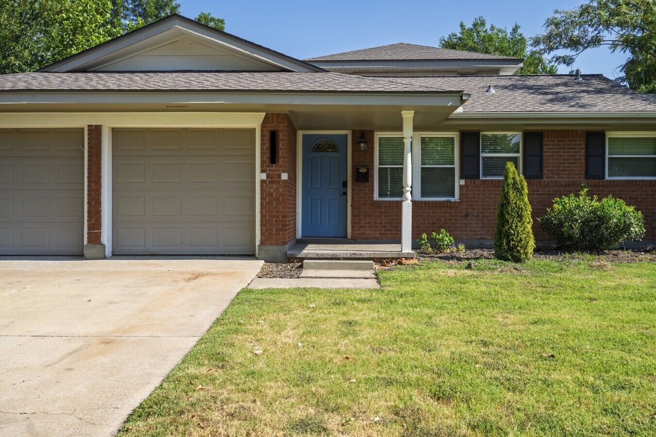 A residential house with a garage, a front door, and a small front yard with grass and a bush.