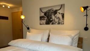 Et hotelværelse med en stor seng, to sengeborde med lamper, et billede af en tyr på væggen og en trædør.