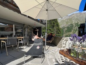 Eine Terrasse mit Tisch, Stühlen, einer Hängematte und einem großen Sonnenschirm.