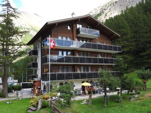 Ein mehrstöckiges Gebäude mit Balkonen, einer Schweizer Flagge und Außenbestuhlung.