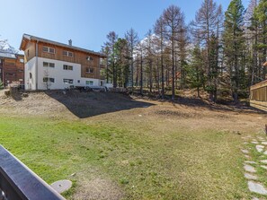 A building with a modern design, a grassy yard, and a forested area with tall trees. - Haus Alfa Appartement/Fewo 804, Vierzimmer Whg by Interhome (Saas-Fee)