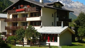 Ein mehrstöckiges Hotel mit Balkonen, einem kleinen Anbau und einem Berg im Hintergrund.