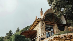 A stone house with a sloped roof, a wooden staircase, and a large window.