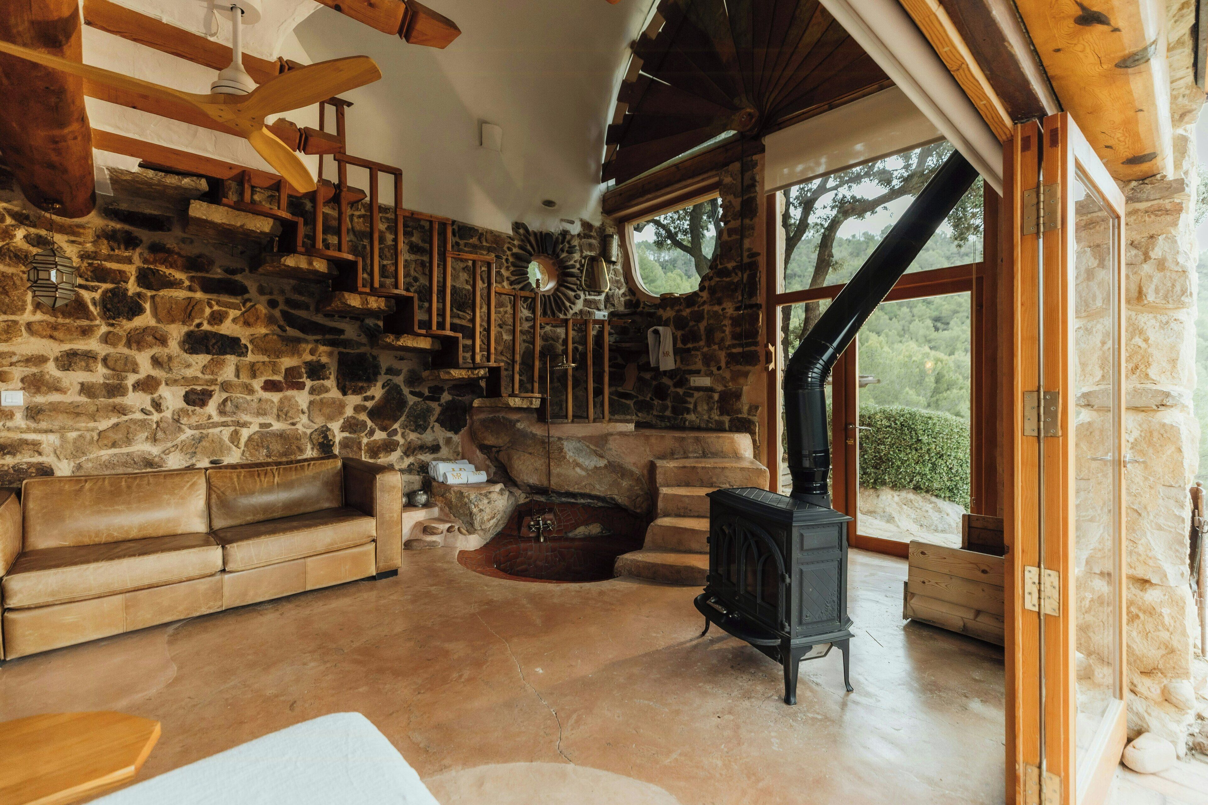 A stone interior with a fireplace, wooden staircase, and a sofa.