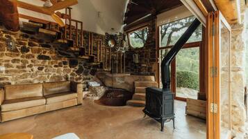 A stone interior with a fireplace, wooden staircase, and a sofa.