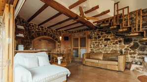 A rustic stone interior with a white sofa, a wooden dining table, and a stone fireplace.