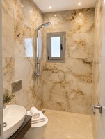 Baño con pared de mármol, ducha, inodoro y lavabo.