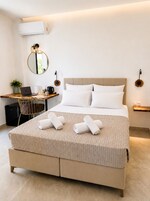 Habitación de hotel moderna con una cama, un escritorio con una computadora portátil, una cafetera y una pequeña planta.