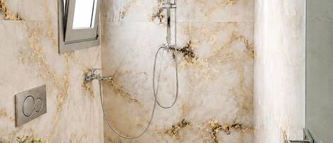 A modern bathroom with a marble wall, a shower, a toilet, and a sink with a towel.