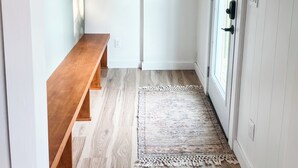 Un couloir avec un banc en bois, un tapis, une porte en bois et une étagère fixée au mur, sur laquelle sont posés divers objets.