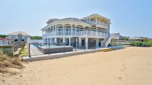 En flervåningsfastighet vid stranden med en pool, en täckt uteplats och en trappa som leder upp till en balkong.