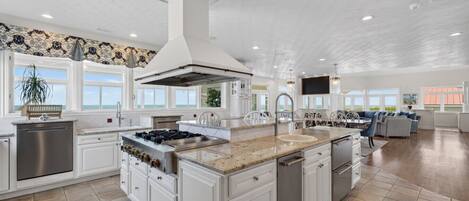 A spacious kitchen with white cabinetry, a large island, stainless steel appliances, and a view of the ocean.