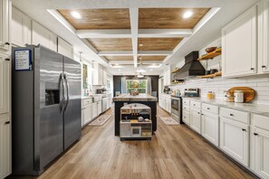 A modern kitchen with white cabinetry, a stainless steel refrigerator, wooden flooring, and a central island with a microwave and oven.
