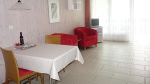 Una camera d'albergo con tavolo, sedie, televisione e una finestra con tende.