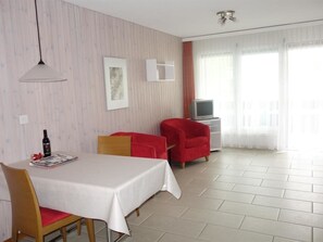 Ein Hotelzimmer mit Esstisch, Stühlen, einem Fernseher und einem Fenster mit Vorhängen.