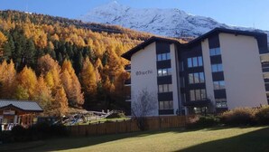 Un edificio con la segnaletica 'Ischi', circondato da alberi autunnali e una montagna innevata.
