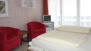 Una camera d'albergo con un letto, due poltrone rosse, una televisione e una libreria.